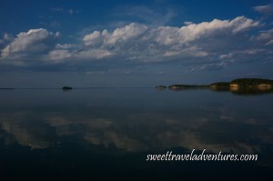 Islands with trees and blue sky with large fluffy white clouds all reflected on calm lake