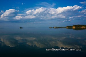 Islands with trees and blue sky with large fluffy white clouds all reflected on calm lake