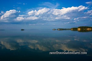Islands with trees and blue sky with large fluffy white clouds all reflected on calm lake