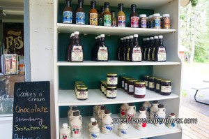 White Shelves With a Dark Green Back Panel and the Top Row of Gordo's Sauces and Spices, Below that a Row of Syrups, Below that a Row of Jams, Below that a Row of Ciders