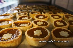 Several Golden-Brown Buttertarts Filled With Orange-Brown Filling and a Flower Shaped Golden-Brown Centre on a Silver Tray
