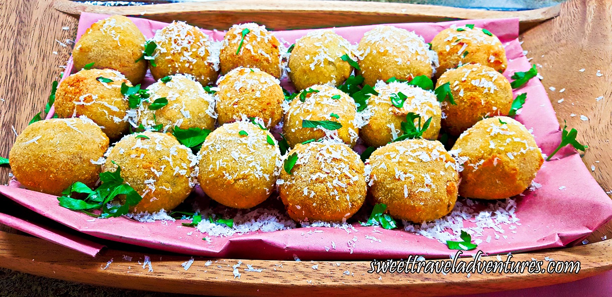 Three Rows of Croquettes on a Piece of Pink Butcher Paper on a Wooden Tray Sprinkled With White Cheese and Garnished With Fresh Parsley