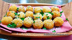 Three Rows of Croquettes on a Piece of Pink Butcher Paper on a Wooden Tray Sprinkled With White Cheese and Garnished With Fresh Parsley