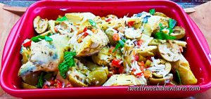 A Large Pink Dish of Artichokes With Mint, Tomatoes, and Olives on a Wooden Tray