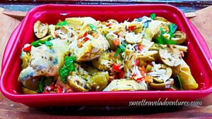 A Large Pink Dish of Artichokes With Mint, Tomatoes, and Olives on a Wooden Tray