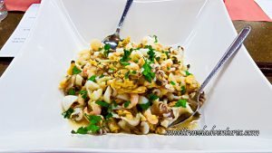 Shrimp, Squid, Clams, Mussels, and Slices of a White Fish With Parsley and a Little Dressing on the Bottom of a White Dish and a Silver Spoon on Either Side of the Dish