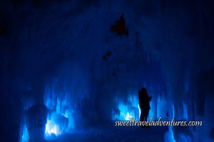 A Silhouette of a Couple Taking a Selfie in an Ice Cavern Partially Illuminated a Lighter Blue at Night