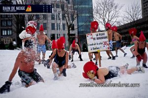 People in Their Bathing Suits Wearing Giant Red Rooster Hats Dancing or Playing in the Snow, a Couple People Hugging Bonhomme, and a Woman Lying Face Down in the Snow