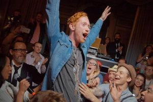 Man Excited With His Arms Raised and Mouth Open and Many Dogtag Necklaces Around His Neck